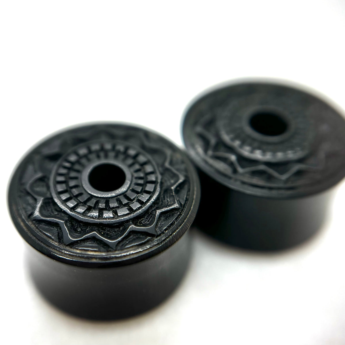 Dark wood double-flare plugs with carved circular patterns and central openings