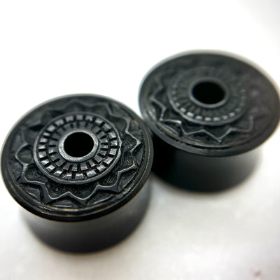 Dark wood double-flare plugs with carved circular patterns and central openings