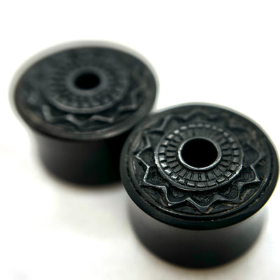 Dark wood double-flare plugs with carved circular patterns and central openings