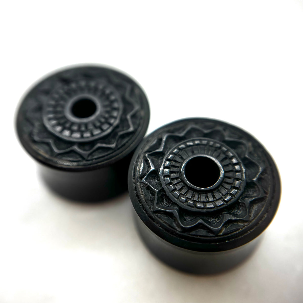 Dark wood double-flare plugs with carved circular patterns and central openings