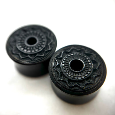 Dark wood double-flare plugs with carved circular patterns and central openings