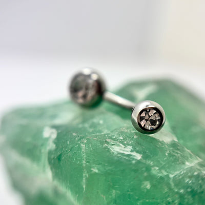 Stainless steel navel bar with clear gemstone ends on green crystal