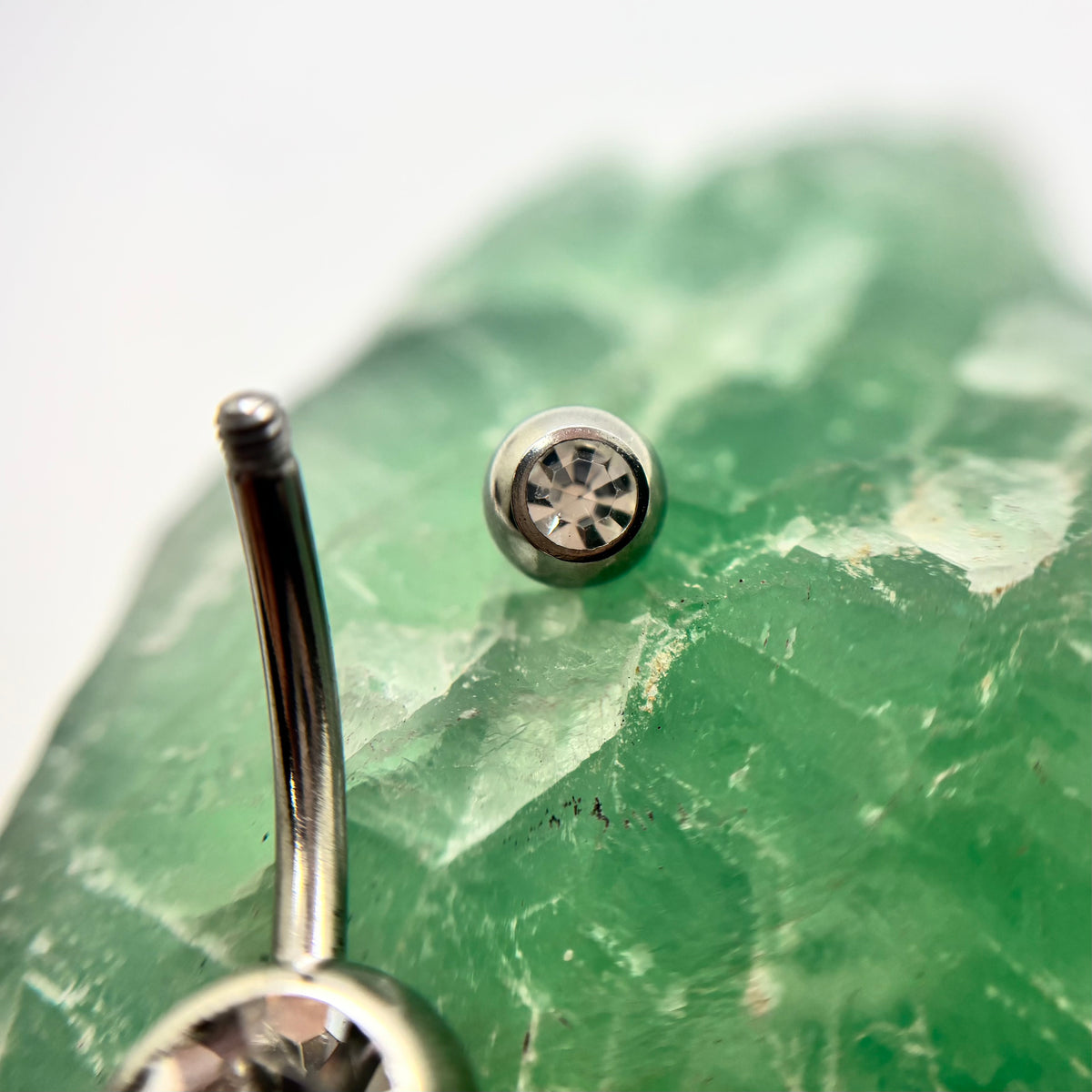 Stainless steel navel bar with a clear gemstone and a removed top bead
