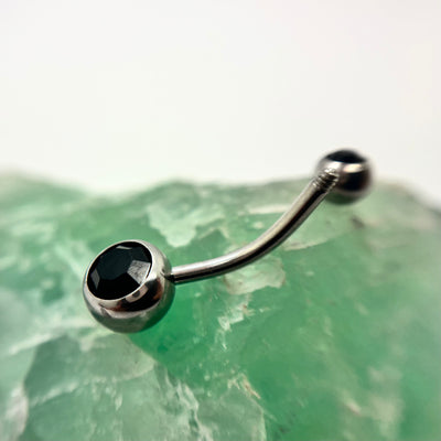 Stainless steel navel bar with black gemstone ends on green crystal