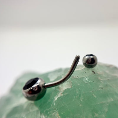 Stainless steel navel bar with black gemstone ends on green crystal