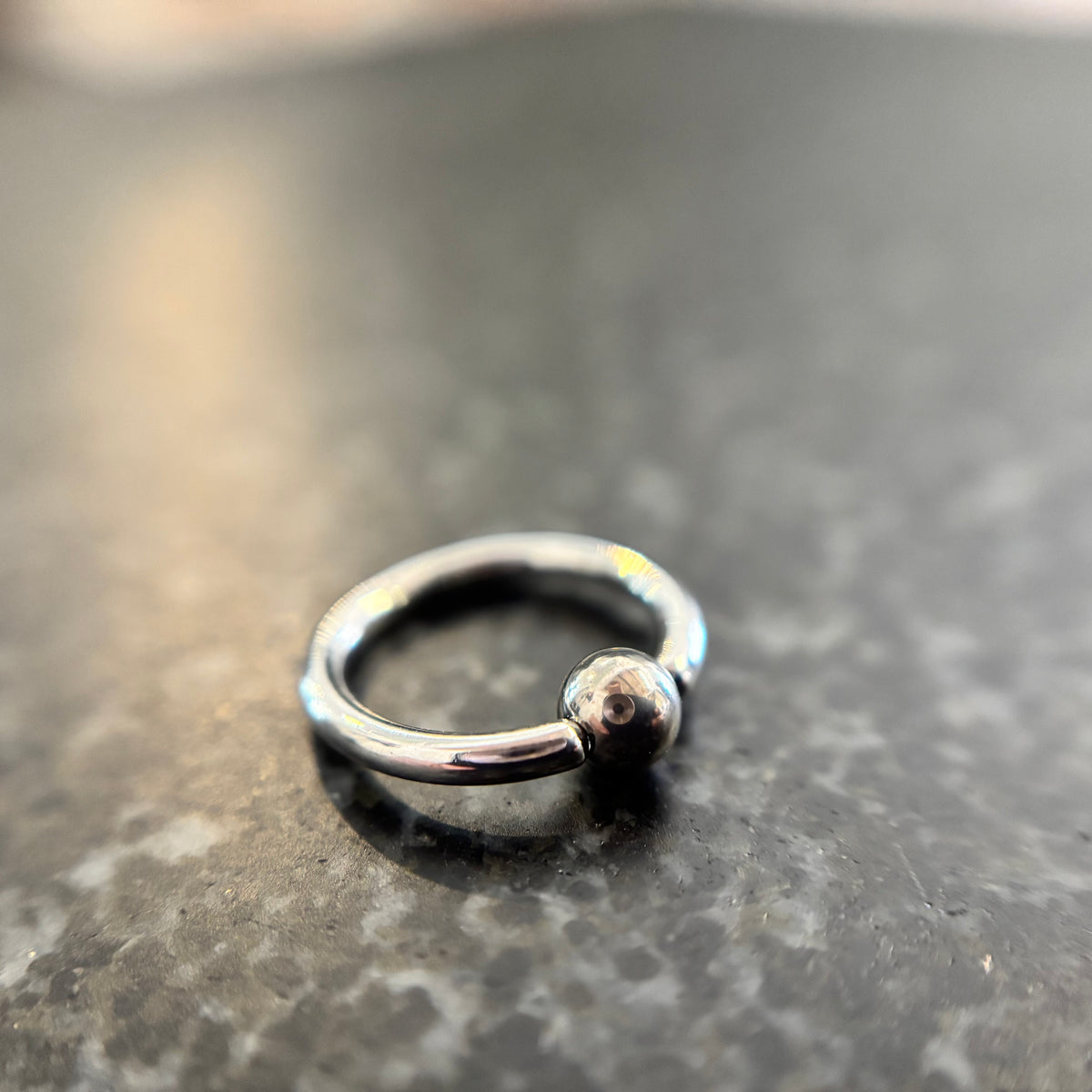 Polished stainless steel captive bead ring on dark stone