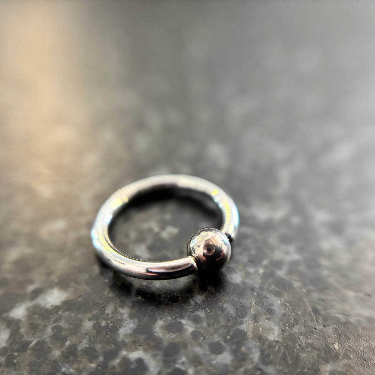 Polished stainless steel captive bead ring on dark stone