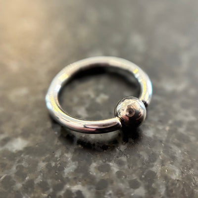 Polished stainless steel captive bead ring on dark stone