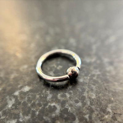 Polished stainless steel captive bead ring on dark stone
