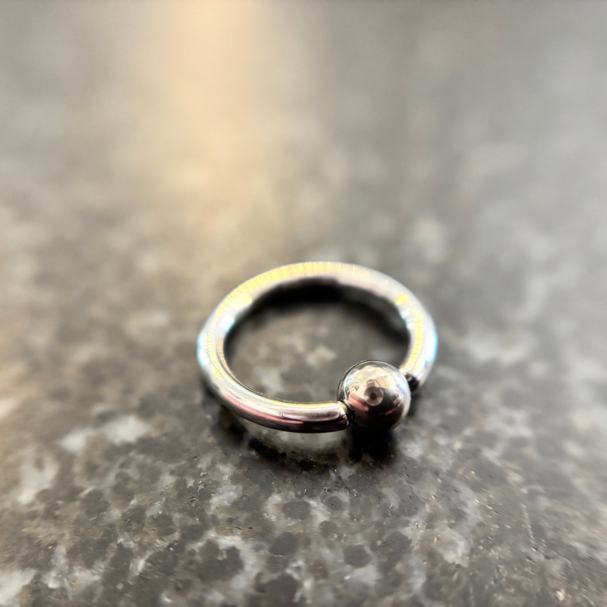 Polished stainless steel captive bead ring on dark stone