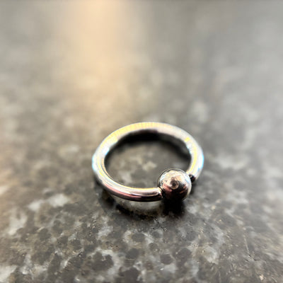 Polished stainless steel captive bead ring on dark stone
