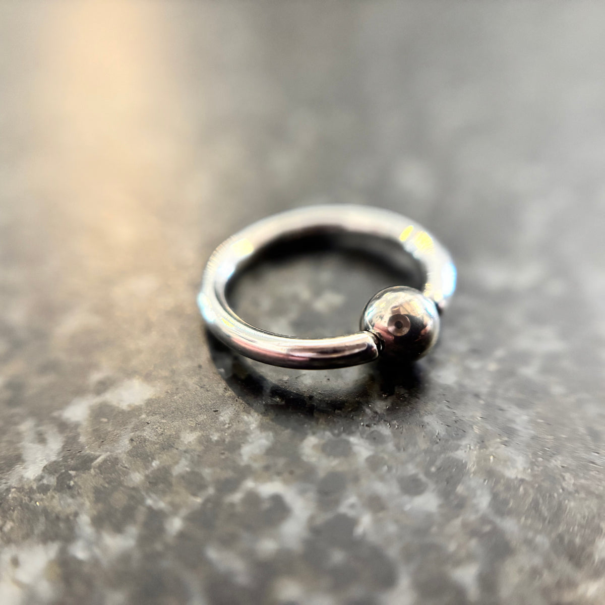 Polished stainless steel captive bead ring on dark stone