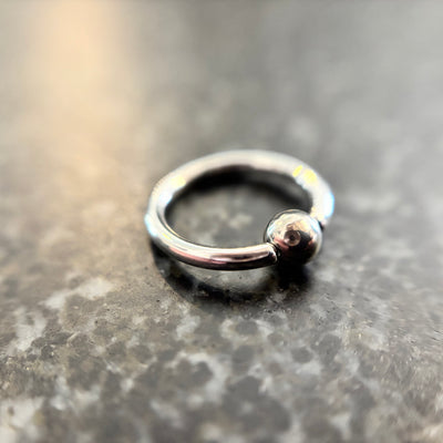 Polished stainless steel captive bead ring on dark stone