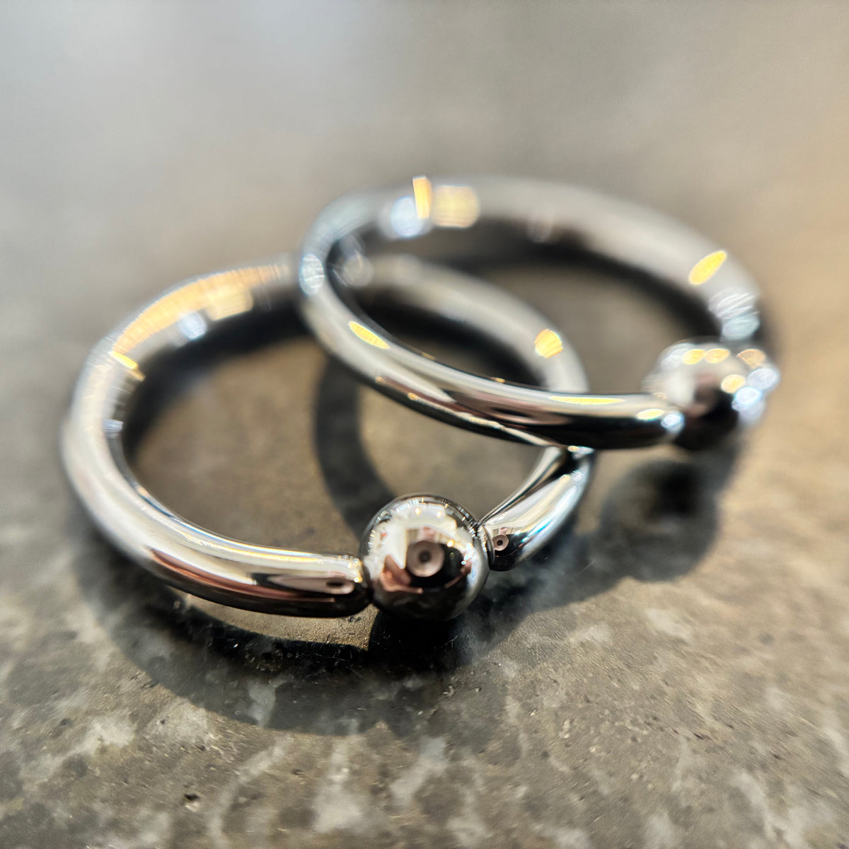 Two overlapping stainless steel captive bead rings on dark stone