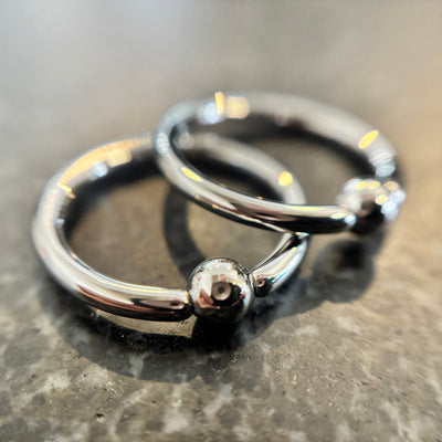Two overlapping stainless steel captive bead rings on dark stone