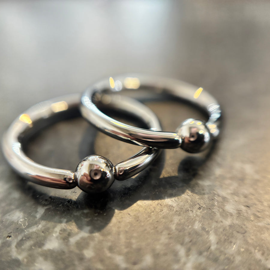 Two overlapping stainless steel captive bead rings on dark stone