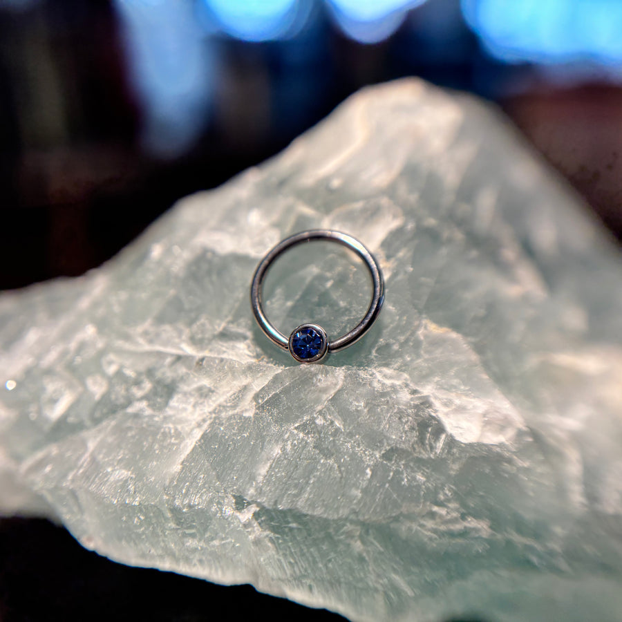 Titanium fixed-bead ring with a blue bead on pale stone