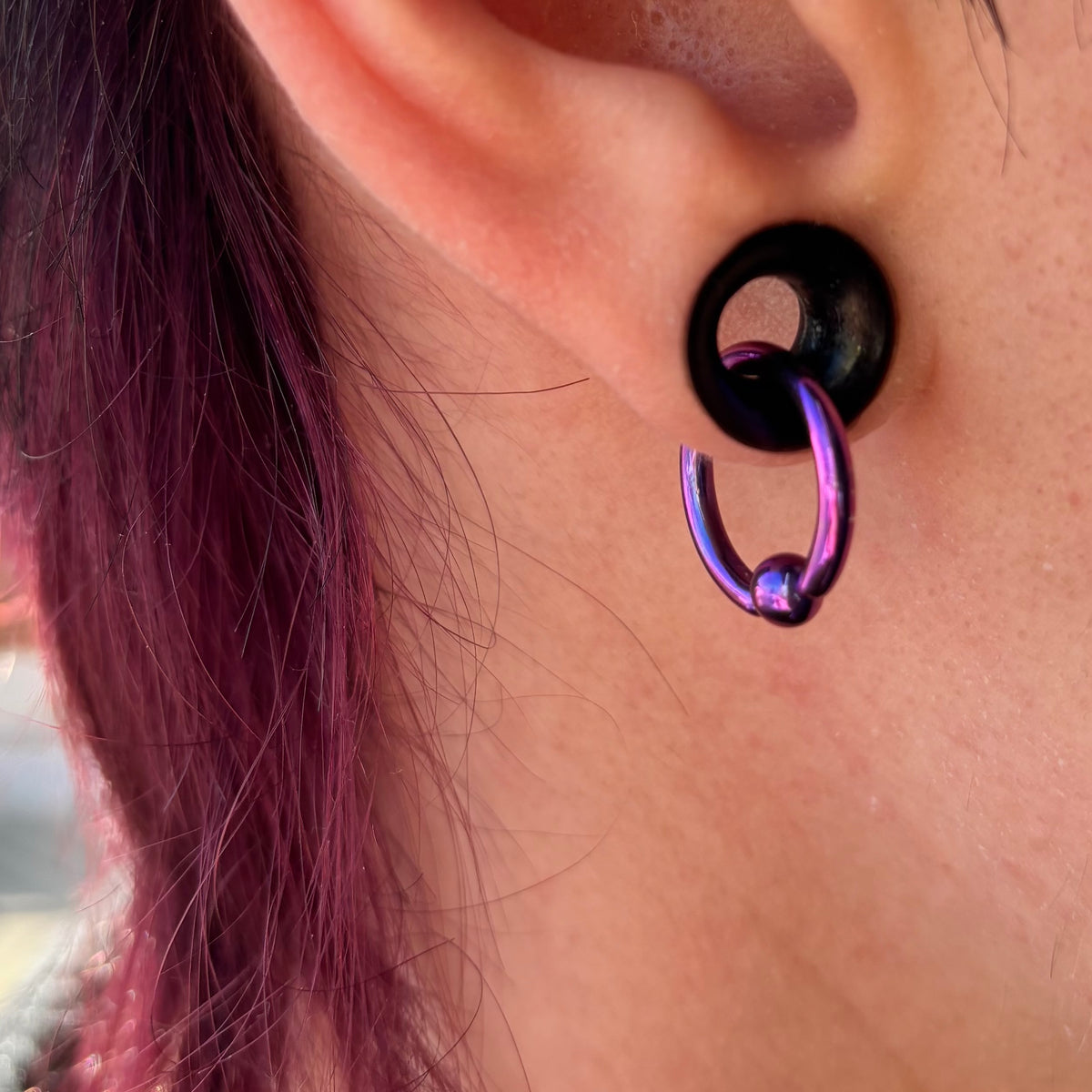 Purple titanium captive bead ring hanging through a black ear tunnel