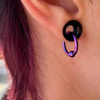 Purple titanium captive bead ring hanging through a black ear tunnel