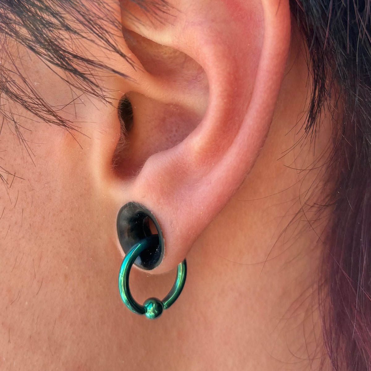 Green titanium captive bead ring hanging through a black ear tunnel