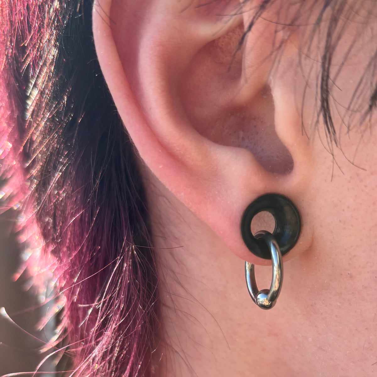Polished titanium captive bead ring hanging through a black ear tunnel