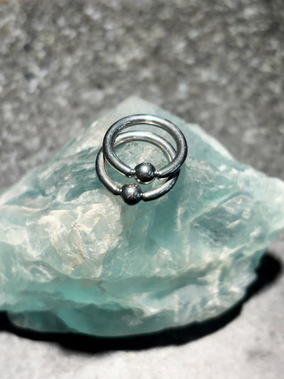 Two polished titanium captive bead rings on pale green stone