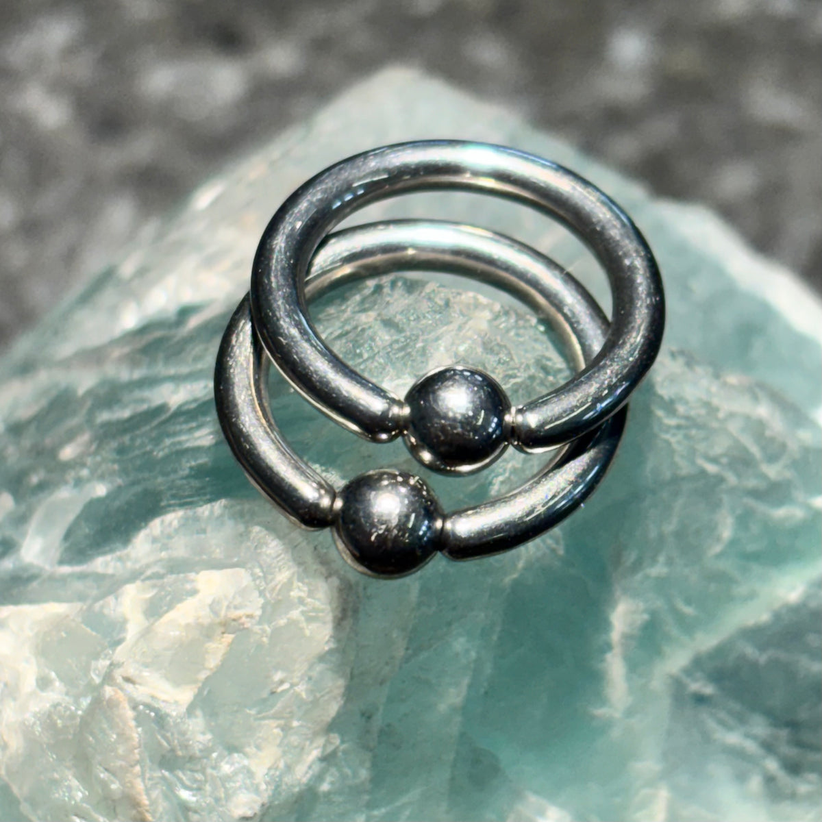 Two polished titanium captive bead rings on pale green stone
