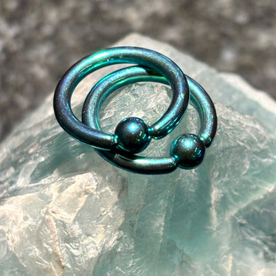 Two green anodized titanium captive bead rings on pale stone