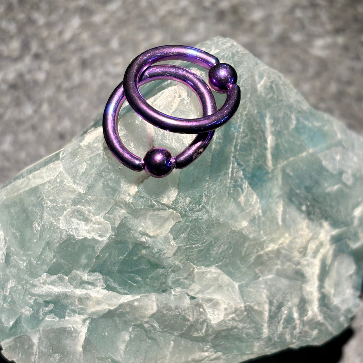 Two purple titanium captive bead rings on pale stone