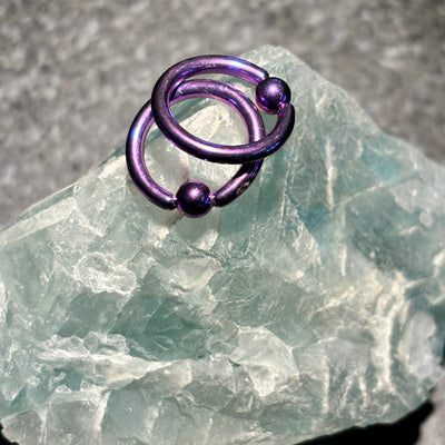 Two purple titanium captive bead rings on pale stone