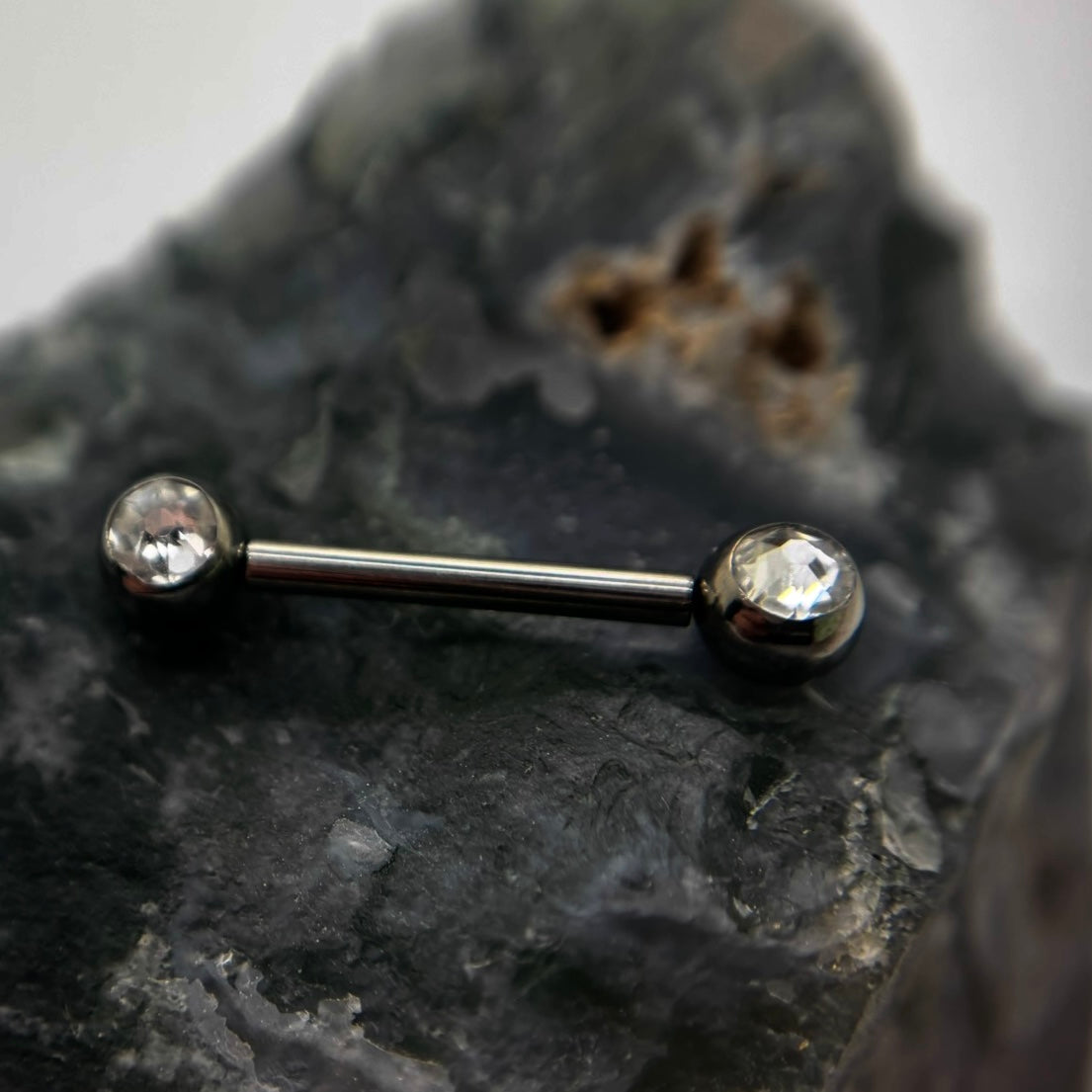 Straight barbell with clear gemstone ends on dark stone