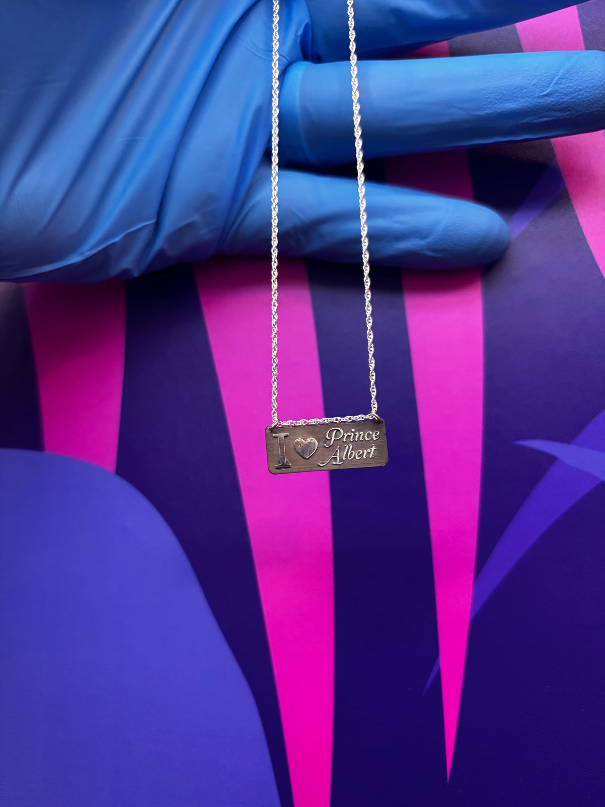 Silver rectangular pendant and chain held in a gloved hand