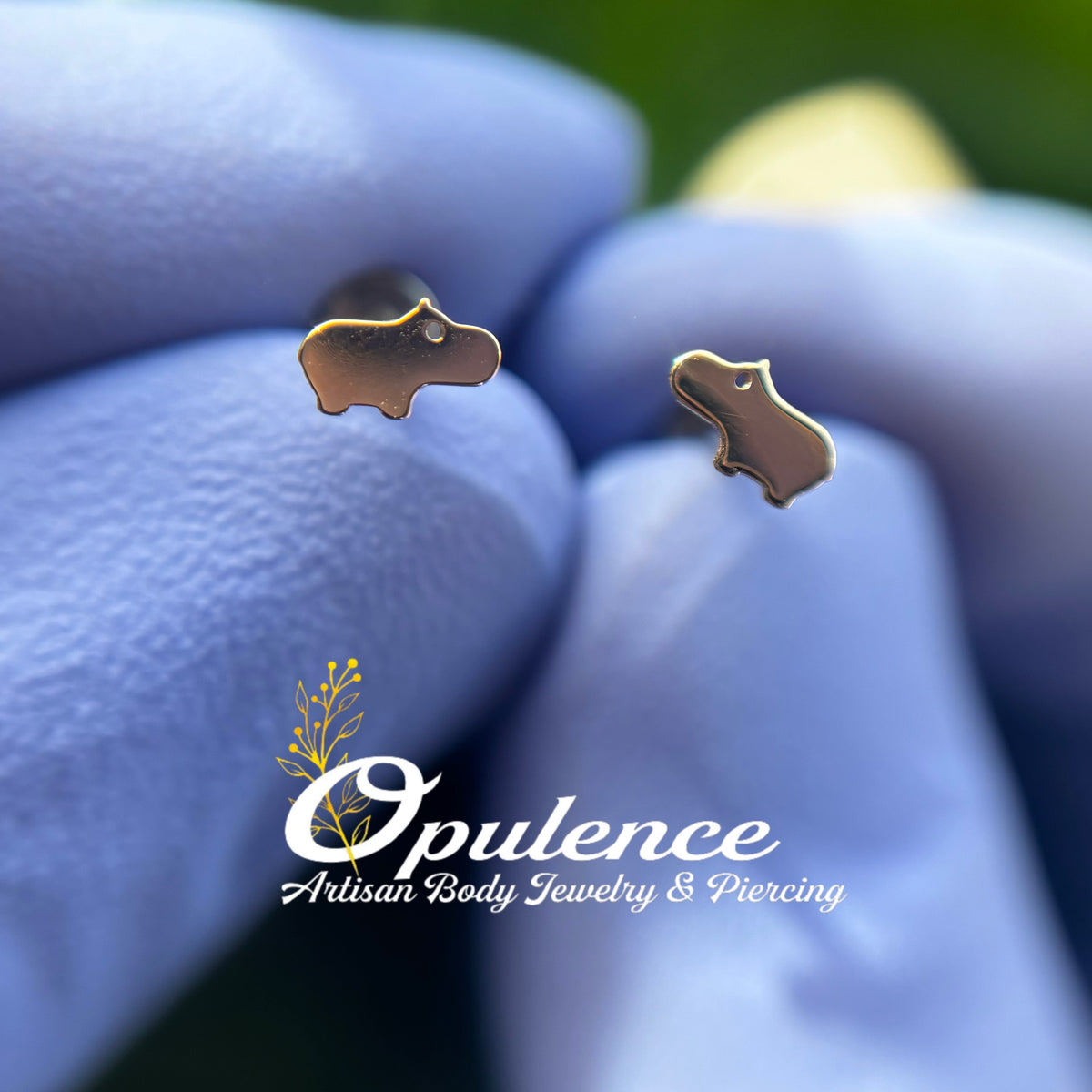 Gold baby hippo-shaped jewelry ends held in gloved fingers
