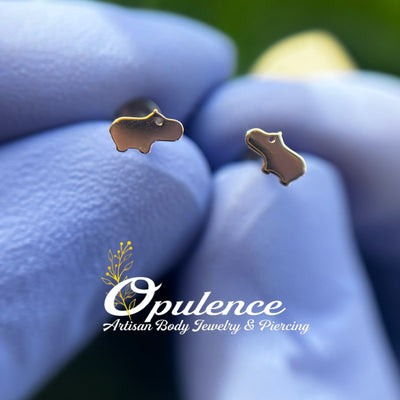 Gold baby hippo-shaped jewelry ends held in gloved fingers