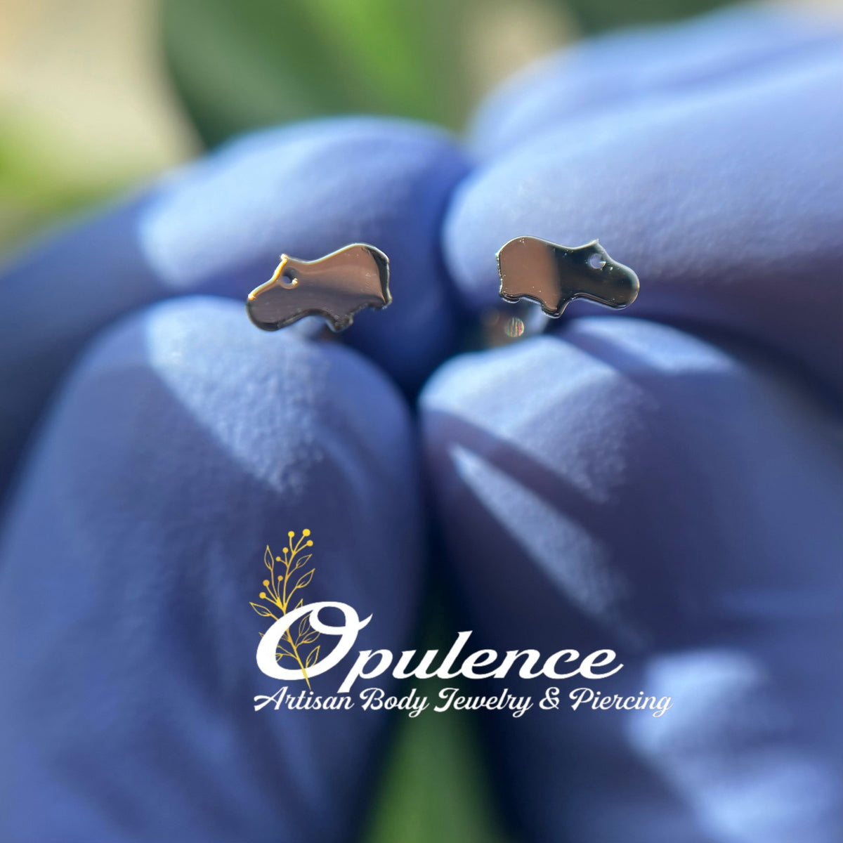 Gold baby hippo-shaped jewelry ends held in gloved fingers