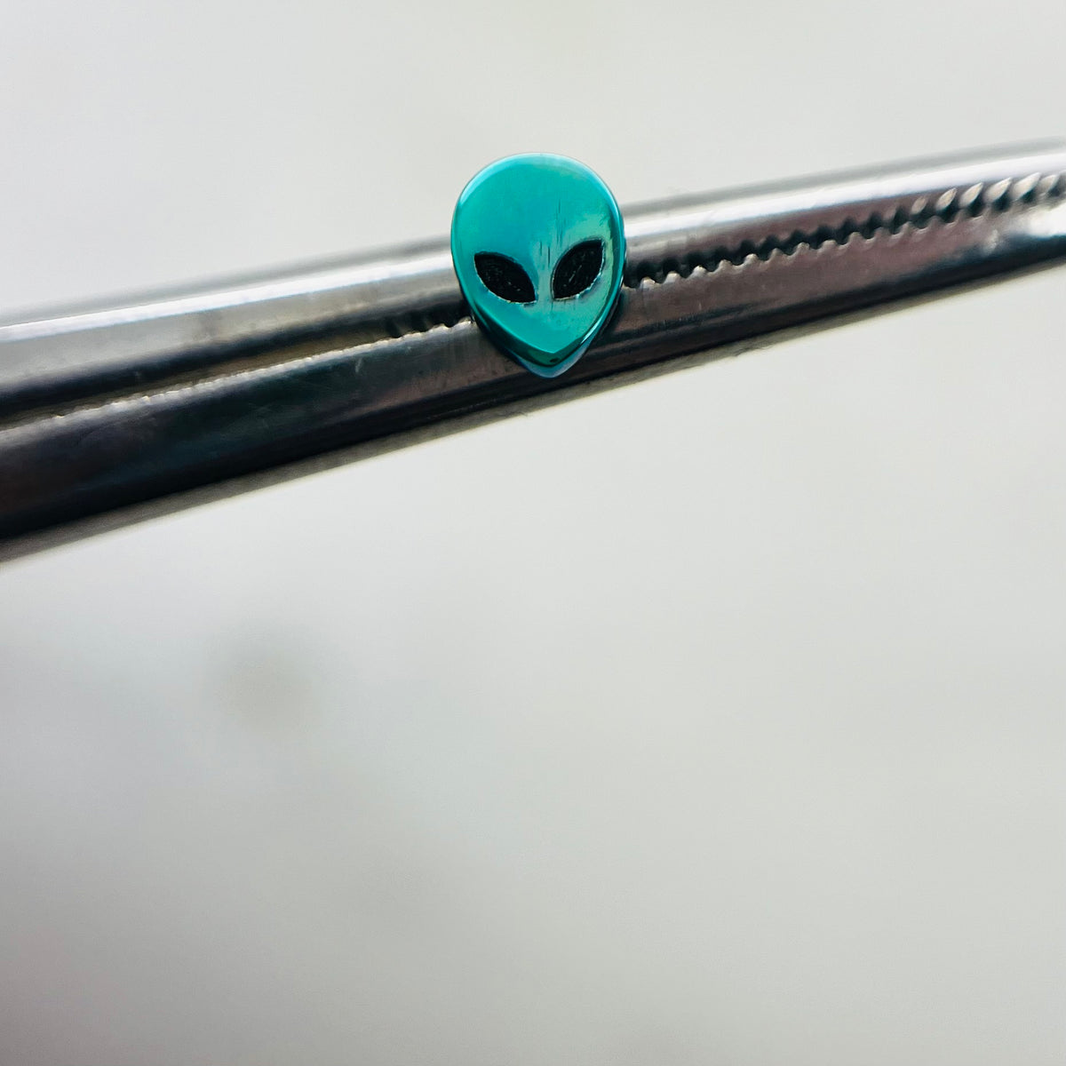 Green titanium alien-head jewelry end held with tweezers
