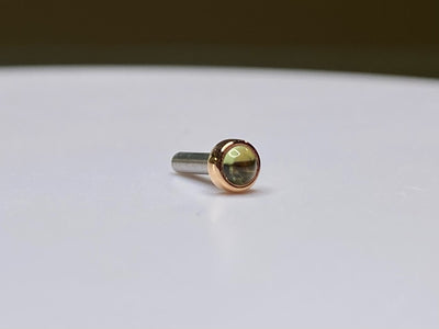 Gold bezel-set peridot stud with its post visible